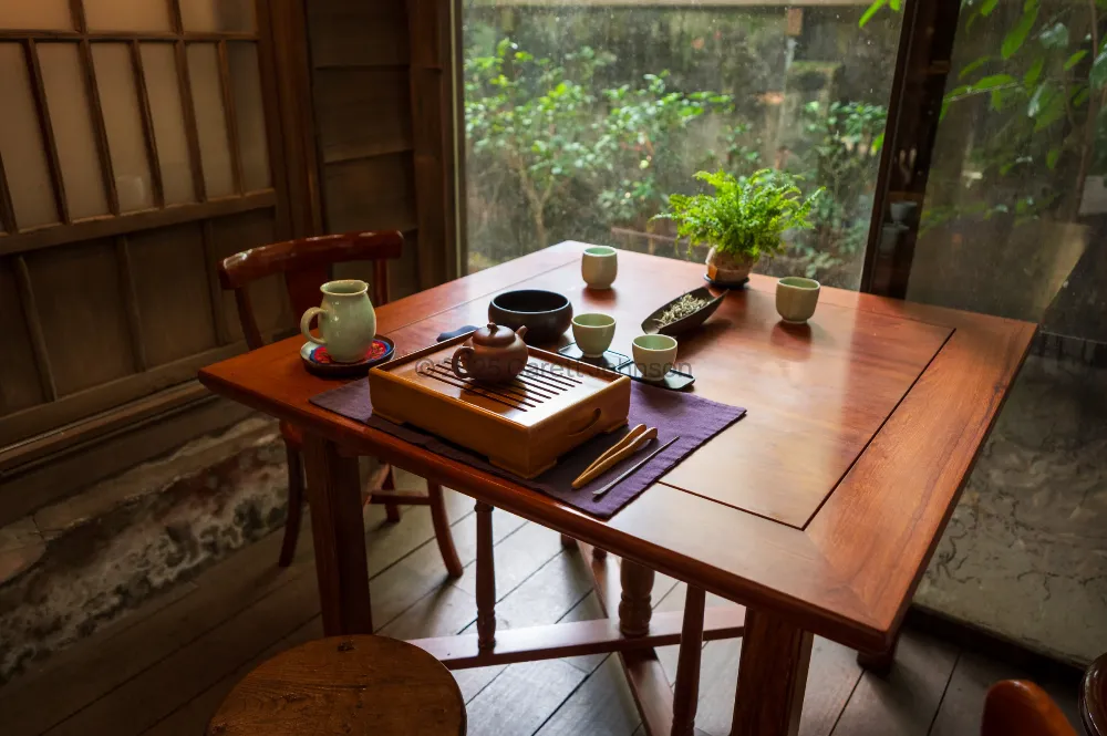 Wooden tea table set with a clay teapot, small cups and a tea tray beside a window onto a rainy green garden in Taipei.