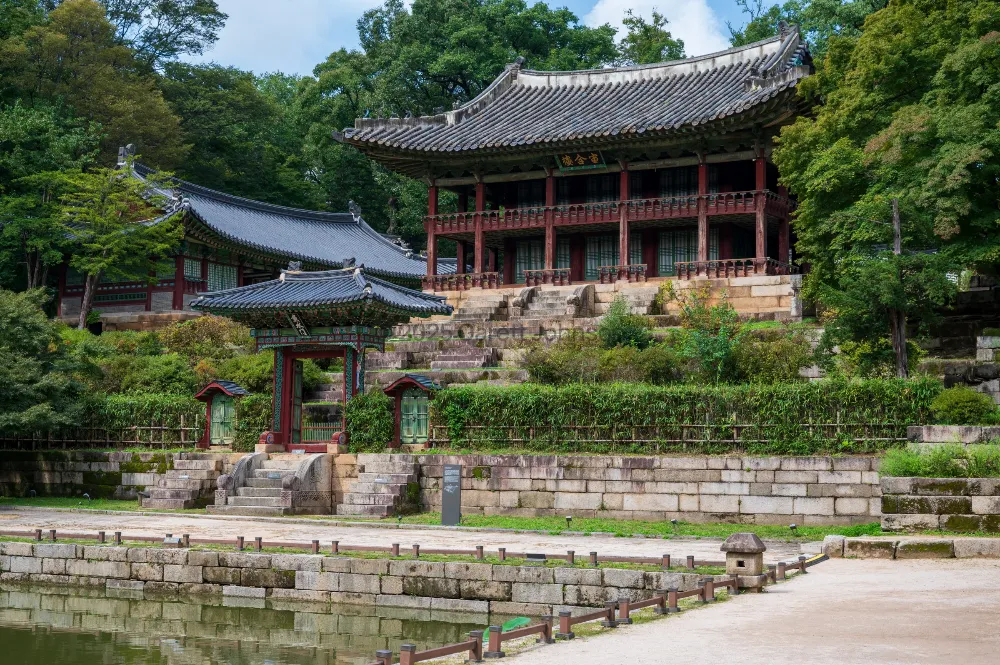 Traditional Korean pavilions with tiled roofs and red pillars rise above stone terraces and a pond at Changdeokgung Palace, Seoul.