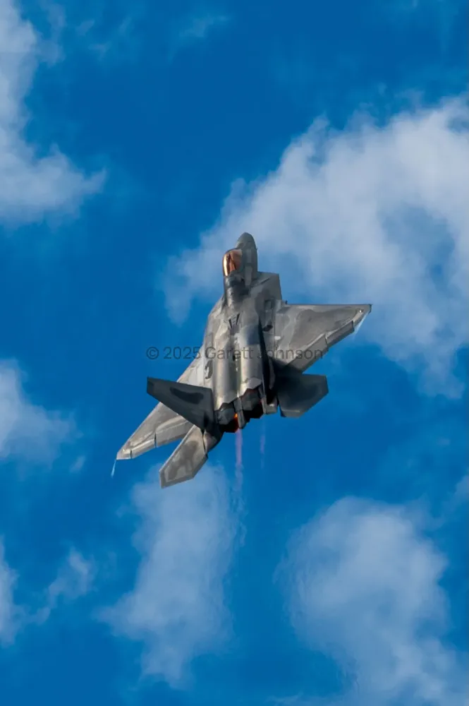 F-22 Raptor climbing vertically against a deep blue sky with afterburner glowing, seen from below at the Duluth airshow.