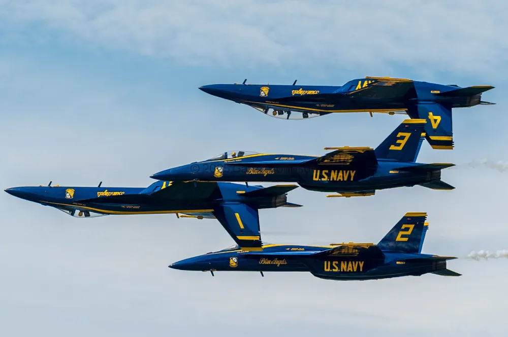 Four Blue Angels jets fly in tight formation against a hazy blue sky, with the top and third jets flying inverted, at the Duluth airshow.