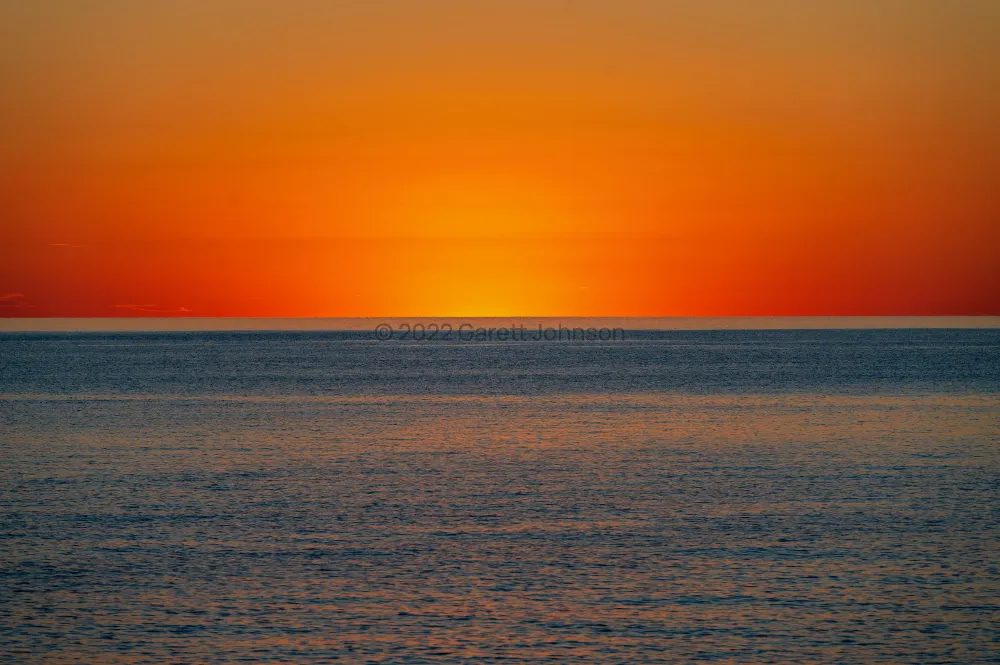 Vivid orange and red sky glowing above the calm, blue-gray water of Lake Superior just before sunrise near Tofte, Minnesota.