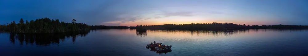 Panoramic aerial view of fishing boats gathered on calm Farm Lake near Ely, MN, under a blue and orange dusk sky